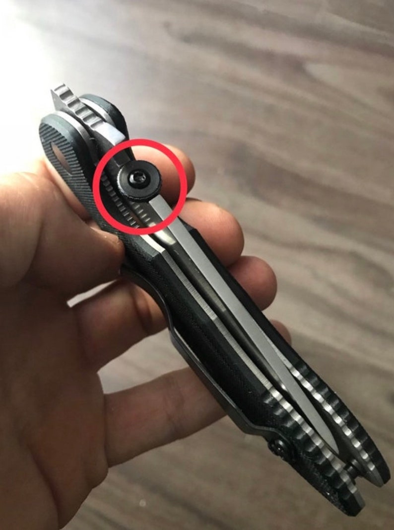 May include: Close-up of a black and silver pocket knife with a textured handle. A small black screw is visible on the side of the knife.