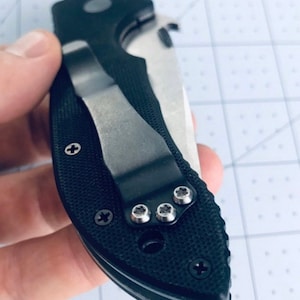 May include: Black pocket knife with a silver clip and a textured black handle. The knife has a silver blade and a silver pocket clip.