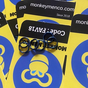 Puede incluir: Varios anillos metálicos azules se muestran sobre una pila de tarjetas amarillas y negras. Las tarjetas presentan un logotipo de pulpo azul y el texto "monkeymenco.com Since 2018". También es visible el texto "Code: FAV18".