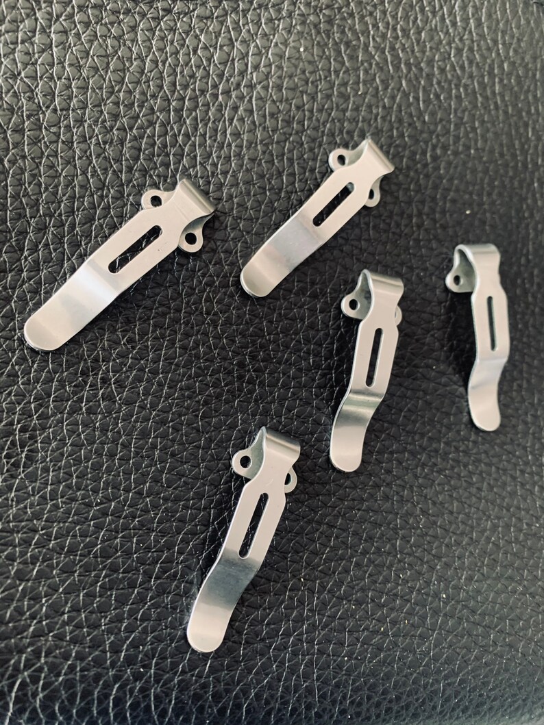 K&ouml;nnte beinhalten: F&uuml;nf silberne Metall-Taschenclips mit einfachem Design. Die Clips sind so konzipiert, dass sie an einer Tasche oder einem G&uuml;rtel befestigt werden k&ouml;nnen.