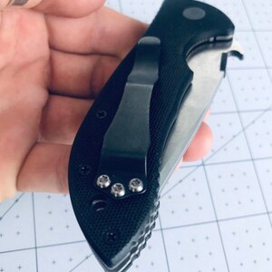 May include: A black pocket knife with a textured handle and a silver blade. The knife has a pocket clip and a small hole for a lanyard.