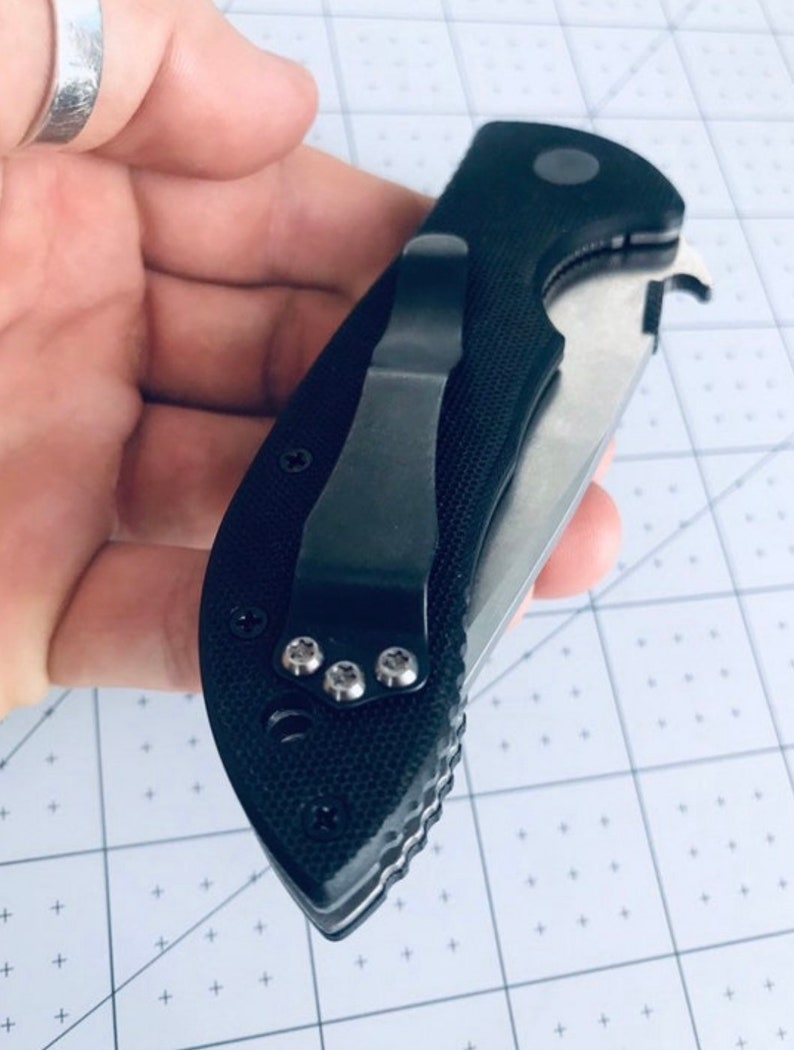 May include: A black pocket knife with a textured handle and a silver blade. The knife has a pocket clip and a small hole for a lanyard.