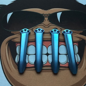 Puede incluir: Cuatro herramientas de titanio azul con punta redondeada y mango texturizado. Las herramientas están dispuestas en fila sobre una superficie marrón.