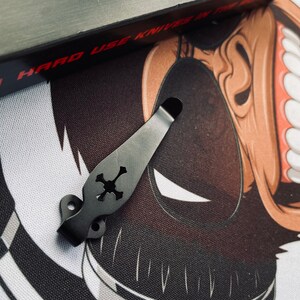May include: Black metal pocket clip with a skull design. The clip is designed to attach to a pocket knife or other tool.