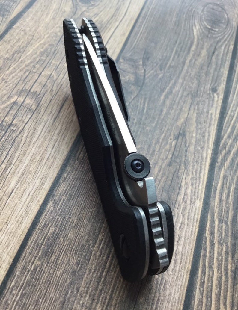May include: A black folding knife with a silver blade and a textured handle. The knife is partially open, showing the blade and the mechanism.