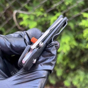 Könnte beinhalten: Ein schwarzes Taschenmesser mit einer silbernen Klinge und einem orangefarbenen Knopf. Das Messer ist geöffnet und die Klinge ist sichtbar.