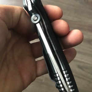 May include: A black folding knife with a silver blade and a textured handle. The knife is partially open, showing the blade and the mechanism.