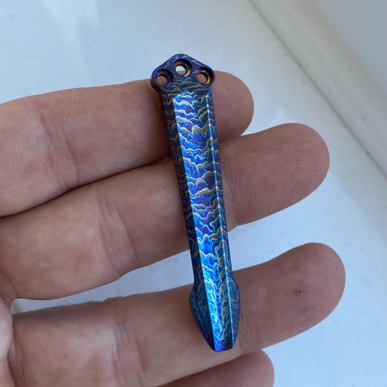 May include: A blue and gold titanium pocket tool with a pointed tip and a three-hole design at the top.