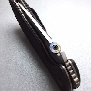 May include: A black and silver folding knife with a partially serrated blade. The knife has a black handle and a silver blade. The blade is partially open, revealing the sharp edge. The knife is designed for everyday carry.