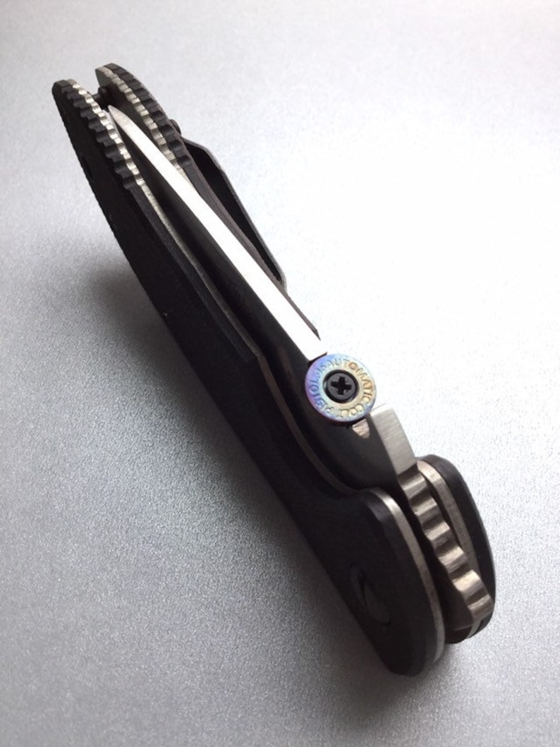 May include: A black and silver folding knife with a partially serrated blade. The knife has a black handle and a silver blade. The blade is partially open, revealing the sharp edge. The knife is designed for everyday carry.