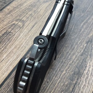May include: A black and silver pocket knife with a textured handle and a partial blade. The knife is closed and has a pocket clip.
