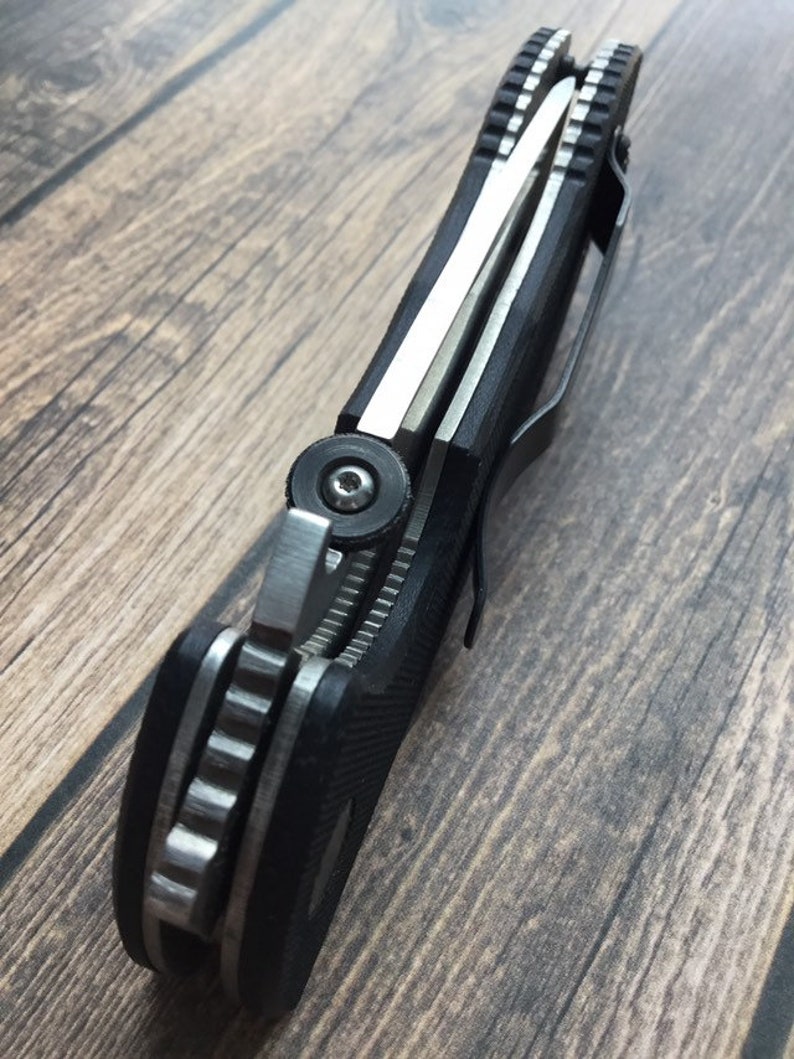 May include: A black and silver pocket knife with a textured handle and a partial blade. The knife is closed and has a pocket clip.