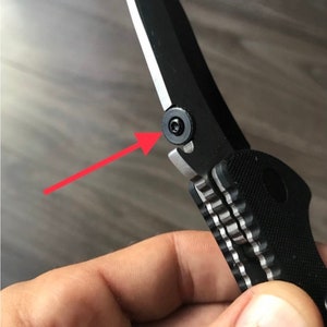 May include: Close-up of a black pocket knife with a silver blade and a textured black handle. A silver screw is visible on the side of the knife.