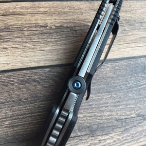May include: A black folding knife with a silver blade and a blue screw. The knife has a textured handle and a pocket clip.