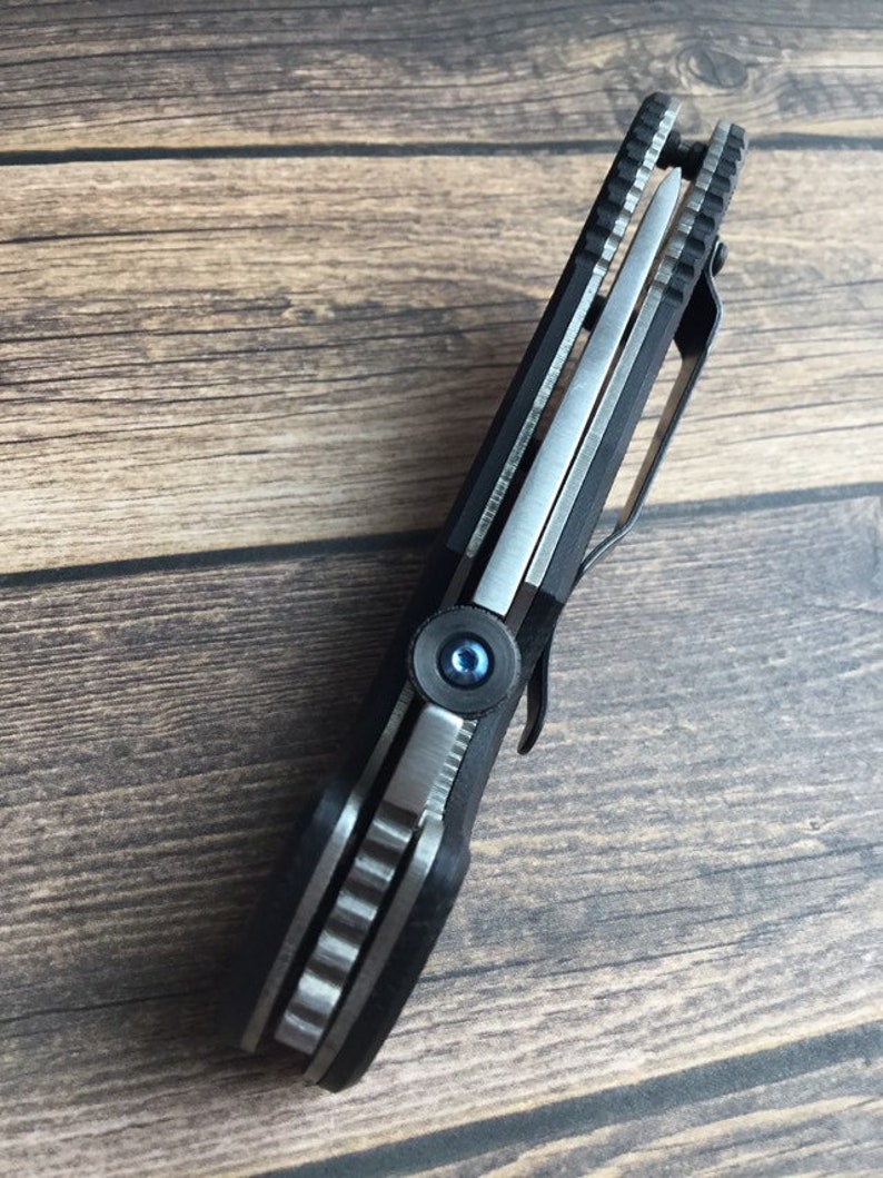 May include: A black folding knife with a silver blade and a blue screw. The knife has a textured handle and a pocket clip.