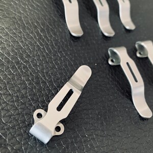 K&ouml;nnte beinhalten: Ein Satz von sieben silbernen G&uuml;rtelschnallen aus Metall. Die Schnallen sind so konzipiert, dass sie an einem G&uuml;rtel befestigt werden und ein Messer oder ein anderes Werkzeug halten.