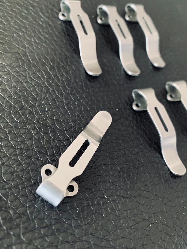 K&ouml;nnte beinhalten: Ein Satz von sieben silbernen G&uuml;rtelschnallen aus Metall. Die Schnallen sind so konzipiert, dass sie an einem G&uuml;rtel befestigt werden und ein Messer oder ein anderes Werkzeug halten.