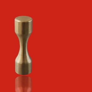 Pode incluir: Um objeto em forma de ampulheta, cor de latão, com parte superior e inferior planas. O objeto está centrado em um fundo vermelho sólido. A forma é simétrica, com uma cintura estreita e extremidades mais largas.