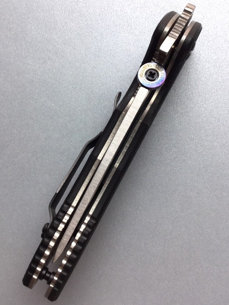May include: A black and silver folding knife with a pocket clip. The knife has a textured handle and a silver blade. The pivot screw has a colorful iridescent finish. The knife is designed for everyday carry.
