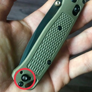 May include: A green and black pocket knife with a textured handle and a silver screw. The knife has a black blade and a silver pocket clip.