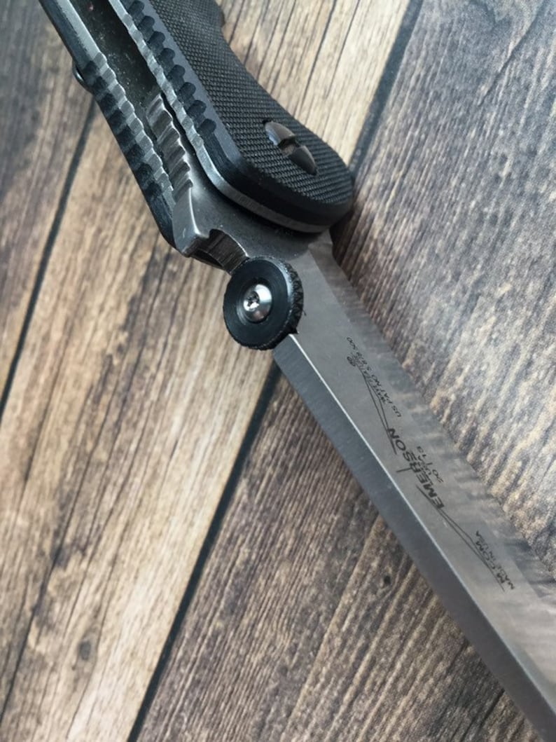 May include: A black and silver folding knife with a textured black handle and a partially open blade. The blade is labeled "Emerson CQC-7K" and "Made in USA".