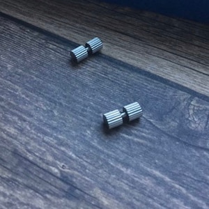 May include: Two silver metal decorative knobs with a ridged design. The knobs are on a wooden surface.