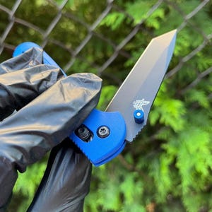 Könnte beinhalten: Ein blaues und schwarzes Taschenmesser mit einer teilweise geöffneten Klinge. Das Messer hat einen blauen Griff und eine schwarze Klinge mit einem silbernen Akzent.