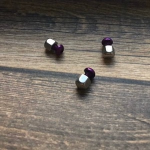 May include: Three silver metal hexagonal nuts with purple plastic tops.