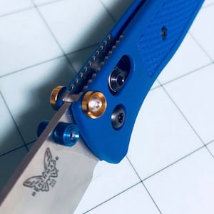 May include: Close-up of a blue pocket knife with a butterfly logo on the blade. The knife has gold and blue accents.