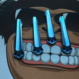 Puede incluir: Cuatro escamas de titanio azul para un cuchillo. Las escamas son lisas y tienen un ligero brillo. Cada escama tiene tres agujeros perforados en la parte inferior.
