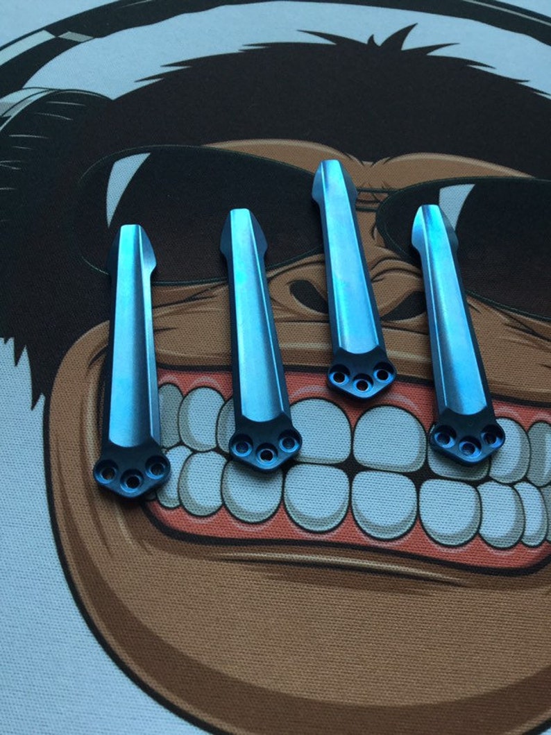 Puede incluir: Cuatro escamas de titanio azul para un cuchillo. Las escamas son lisas y tienen un ligero brillo. Cada escama tiene tres agujeros perforados en la parte inferior.