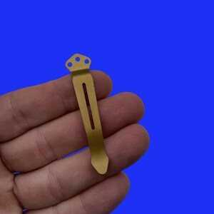 Pu&ograve; includere: Un fermaglio da tasca in metallo dorato con punta arrotondata e tre fori nella parte superiore.