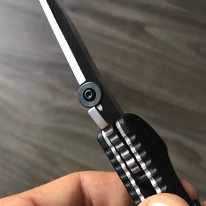 May include: A black folding knife with a partially extended blade. The knife has a black handle with a silver accent and a silver pivot screw.