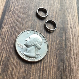 May include: Close-up of a silver quarter coin with the profile of George Washington and the years 1776-1976. Two small, silver split rings are next to the coin on a wooden surface. The rings are made of three connected loops.