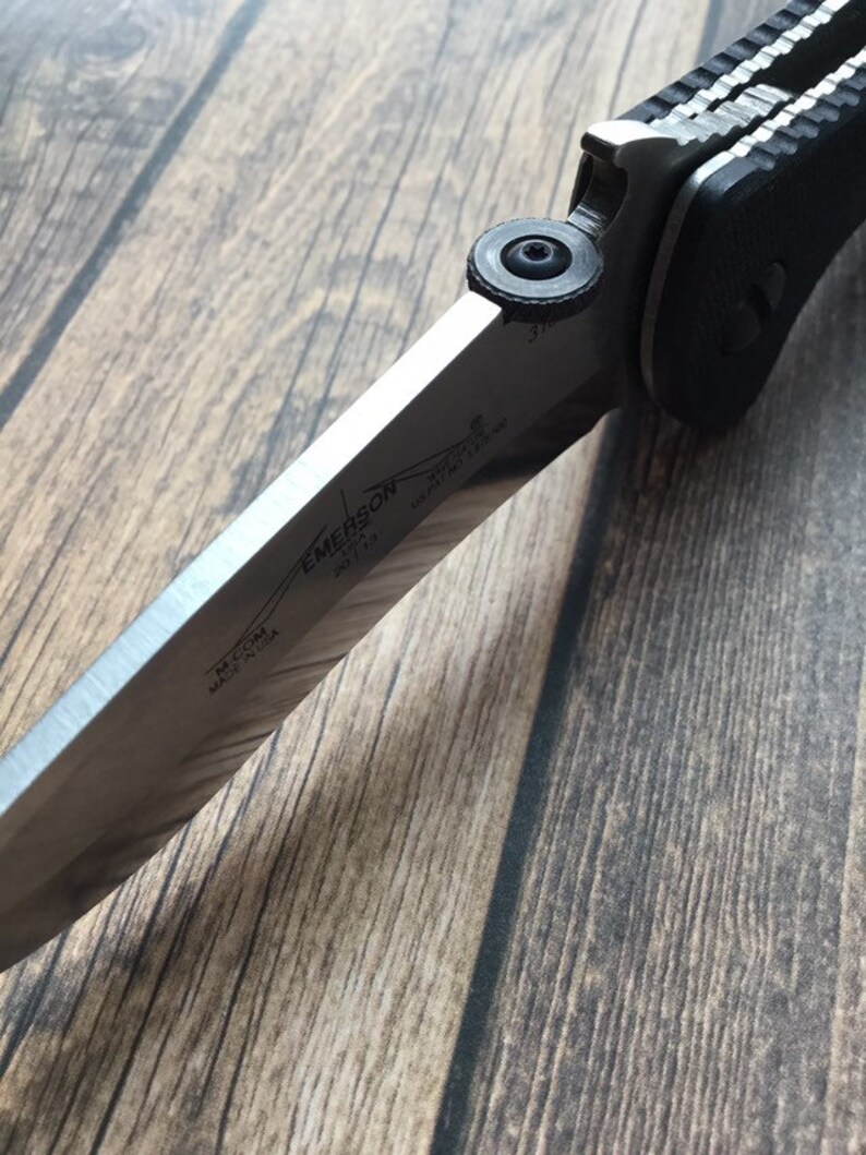 May include: A silver folding knife with a black handle. The blade has the text "EMERSON KNIVES" and "MADE IN USA" on it.