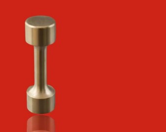 May include: A single, metallic gold dumbbell against a vibrant red background. The dumbbell has a cylindrical handle connecting two circular weights. The image is well-lit, highlighting the dumbbell's shape and colour.