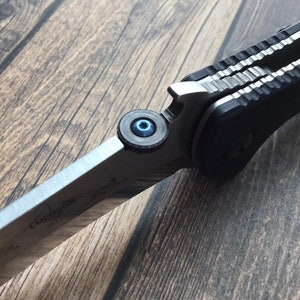 May include: Close-up of a silver pocket knife with a black handle and a blue screw. The knife is partially open, revealing the blade.