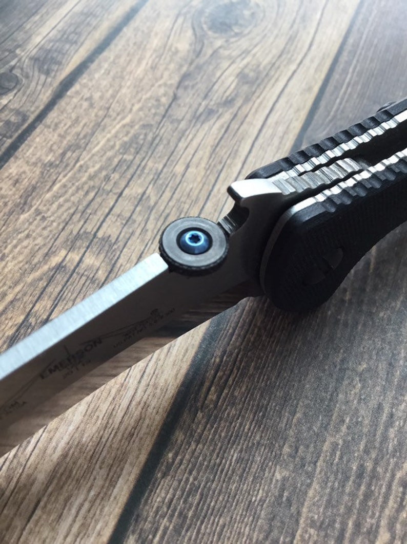May include: Close-up of a silver pocket knife with a black handle and a blue screw. The knife is partially open, revealing the blade.