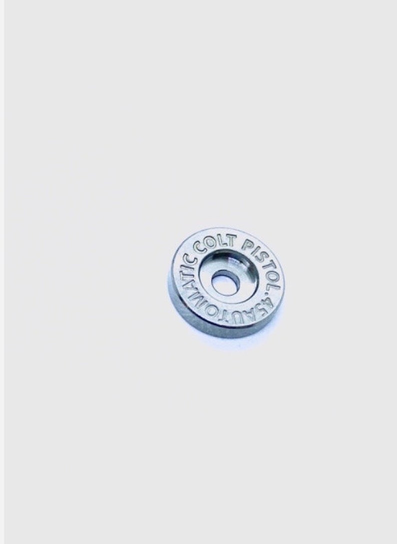 May include: A silver-colored metal disc with the words "AUTOMATIC COLT PISTOL" engraved around the edge.