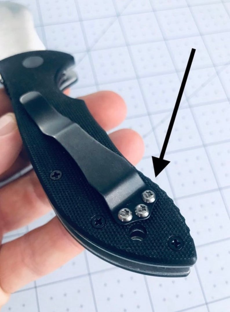 May include: A black pocket knife with a black clip and a textured handle. The clip is attached to the handle with four silver screws.