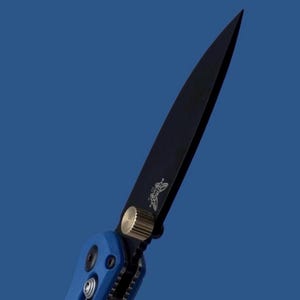 Peut inclure: Un couteau de poche pliant doté d'une lame pointue noir mat arborant un petit logo papillon. Le manche est bleu vif avec une surface texturée et comprend un bouton de pouce circulaire de couleur or métallique pour ouvrir le mécanisme.