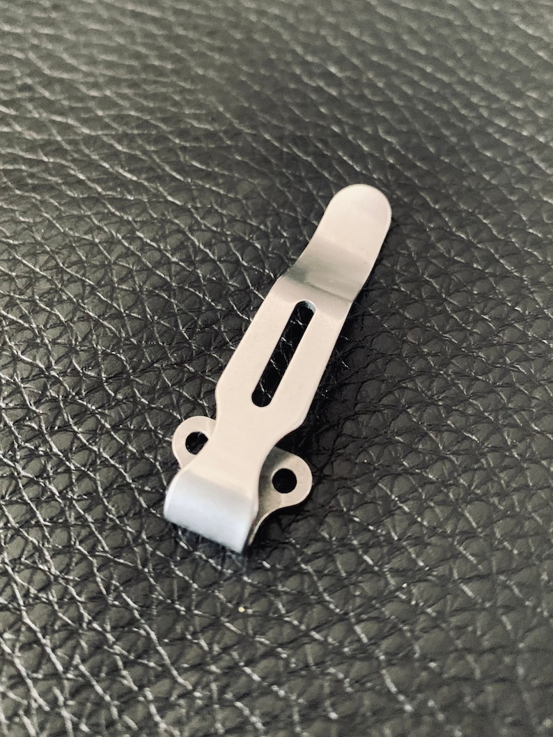 K&ouml;nnte beinhalten: Ein silberner Metall-Taschenclip mit zwei L&ouml;chern an der Seite und einem Schlitz in der Mitte.