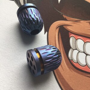 Op de afbeelding: Twee blauwe en paarse metalen fidget-speeltjes met een getextureerd oppervlak. Een speelgoed heeft een gouden ring rond het midden.