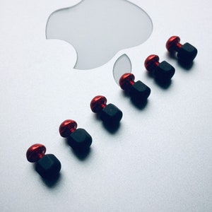May include: Six red and black metal knobs with a hexagonal base. The knobs are arranged in a line on a silver surface.