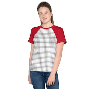 May include: A red and white grid pattern t-shirt with red sleeves. The shirt is worn with blue jeans. The grid pattern is black and white. The model is smiling.