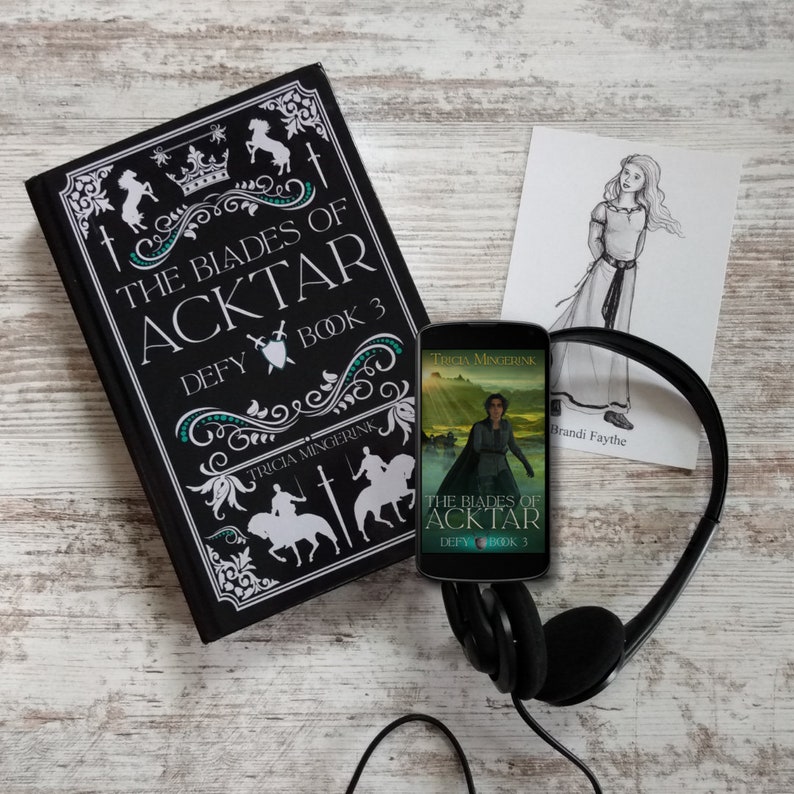 Puede incluir: Un libro negro de tapa dura titulado "The Blades of Acktar Defy Book 3" de Tricia Mingerink. Un tel&eacute;fono inteligente negro con una ilustraci&oacute;n de portada similar est&aacute; al lado del libro. Un par de auriculares negros est&aacute;n sobre la mesa. Una ilustraci&oacute;n en blanco y negro de una ni&ntilde;a con un vestido est&aacute; en una tarjeta blanca.