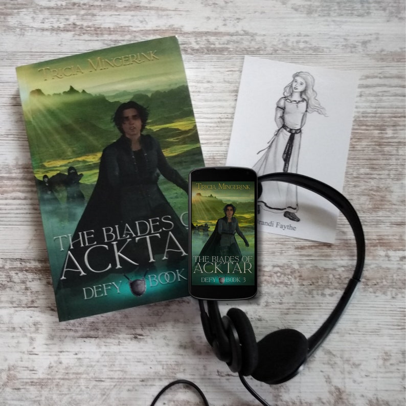 Puede incluir: Un libro de bolsillo titulado "The Blades of Acktar: Defy Book 3" de Tricia Mingerink. La portada muestra a una mujer con una capa negra de pie en un paisaje verde. Un tel&eacute;fono inteligente con la misma portada de libro est&aacute; al lado del libro. Los auriculares est&aacute;n sobre una superficie de madera blanca.