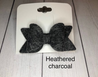 May include: A gray felt hair bow with a textured, fuzzy finish. The bow is on a white card with the text "Heathered charcoal".