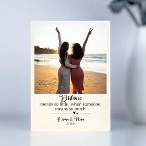 May include: A photo of two friends on a beach with the quote "Distance means so little, when someone means so much." and the names "Emma & Nora" and the year "2024" below the photo.