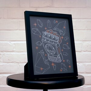 May include: A black framed print with a white illustration of a hand wearing a spiked gauntlet. The gauntlet is surrounded by white geometric shapes on a dark gray background.